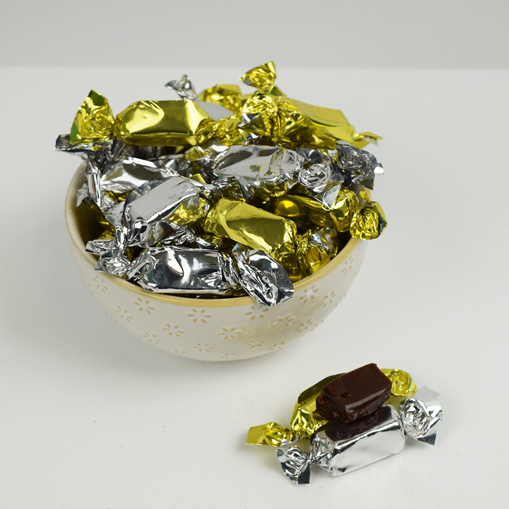 Bowl filled with gold and silver wrapped coffee prims on a white background