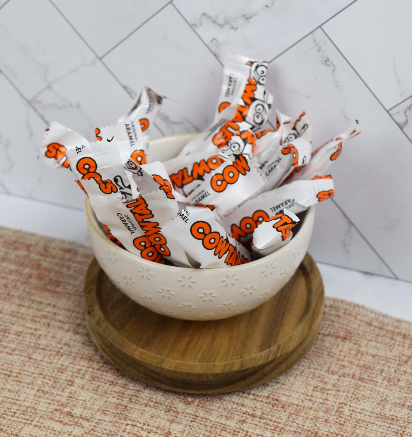 Bowl filled with Cow Tales Minis candy bars on a textured surface with a tiled wall background
