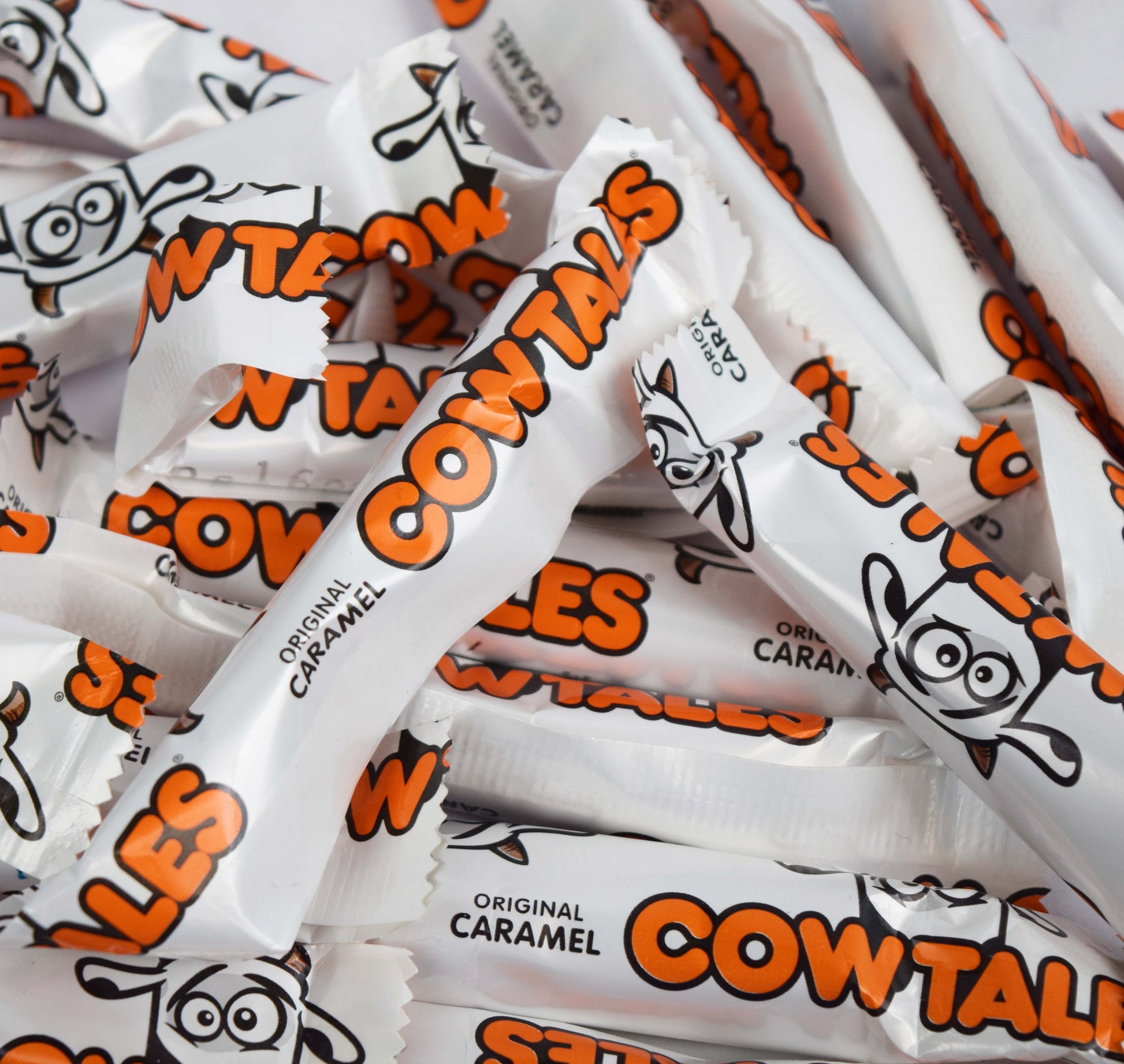 Pile of Cow Tales candy bars with orange and black text and cartoon cows.