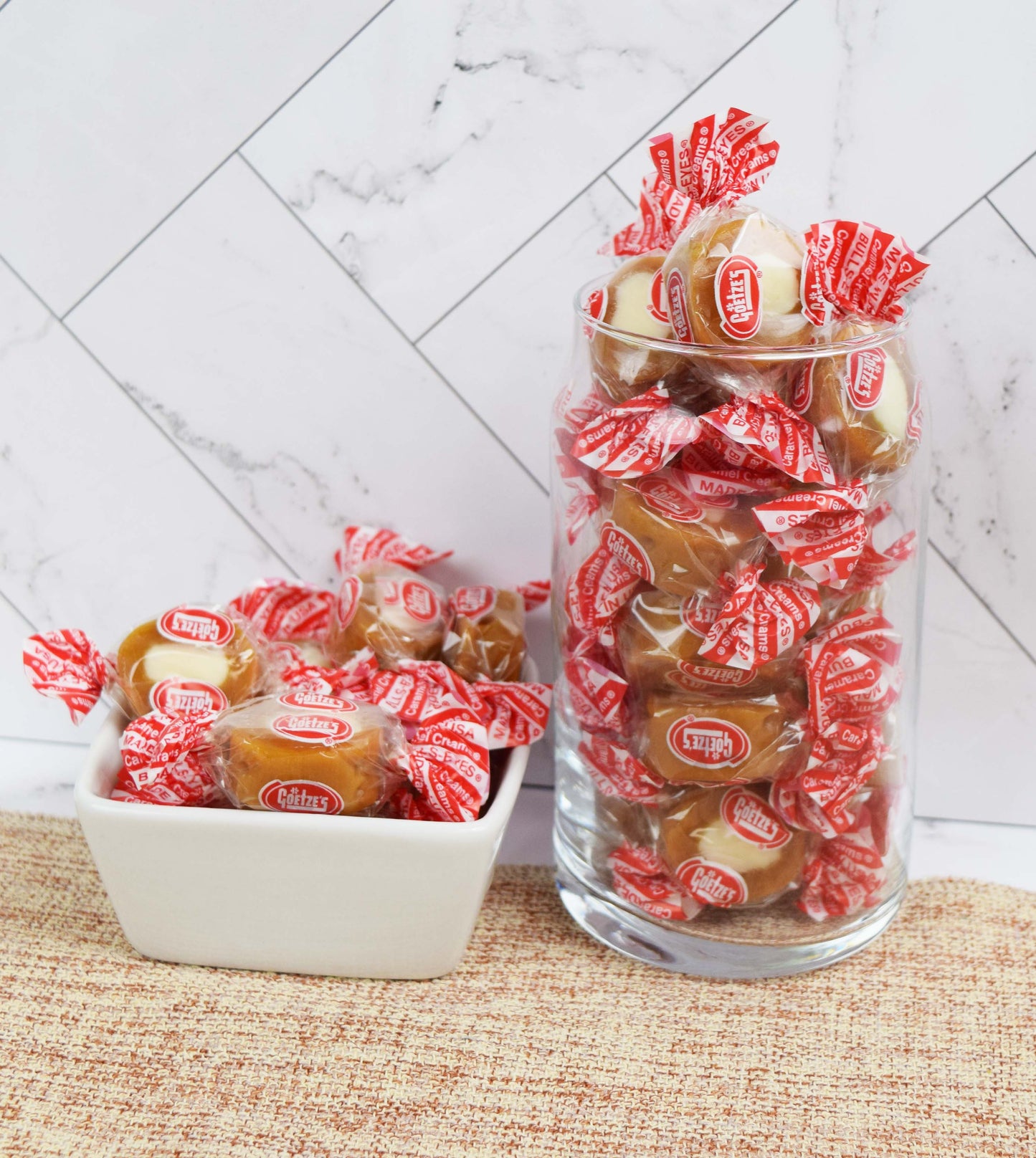 Jar and bowl filled with Goetze's Caramel Creams on a marble wall background
